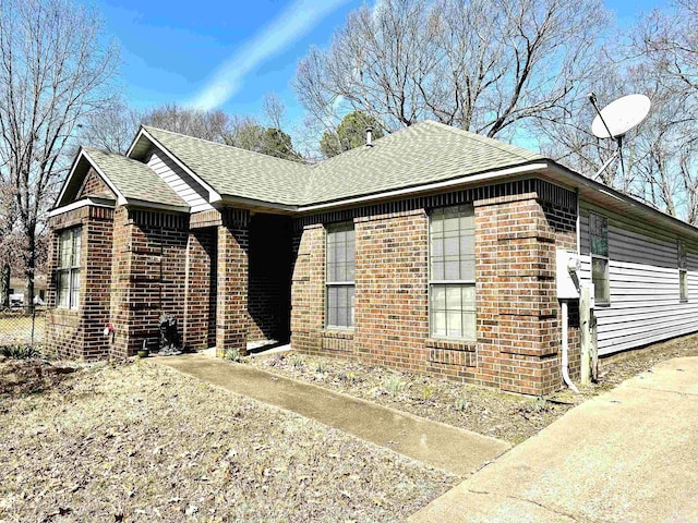 view of property exterior featuring brick siding and a shingled roof