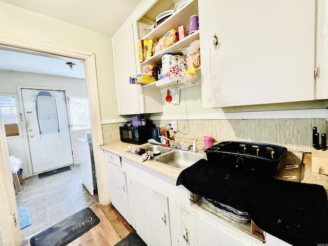 kitchen with a sink, open shelves, white cabinetry, black microwave, and light countertops