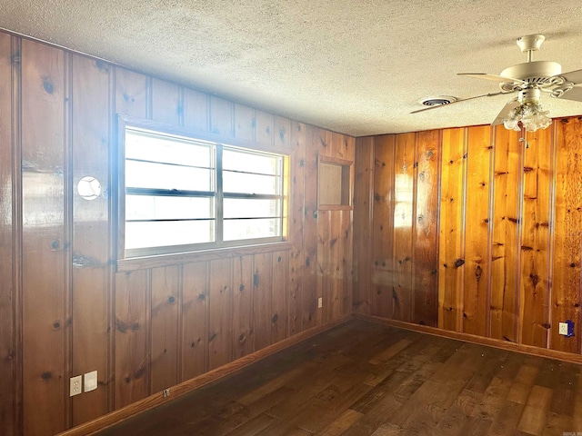 unfurnished room with a textured ceiling, wood finished floors, wood walls, baseboards, and ceiling fan