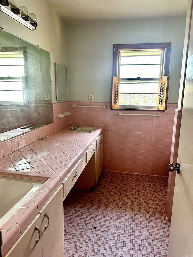 full bath with double vanity, plenty of natural light, tile walls, and a wainscoted wall