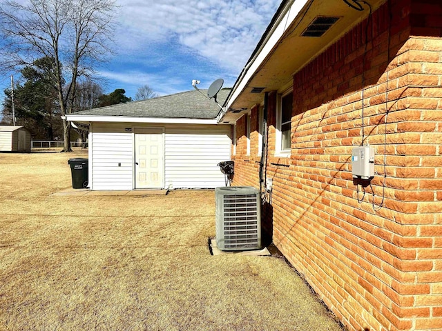 view of side of home with brick siding, roof with shingles, cooling unit, an outbuilding, and a storage unit