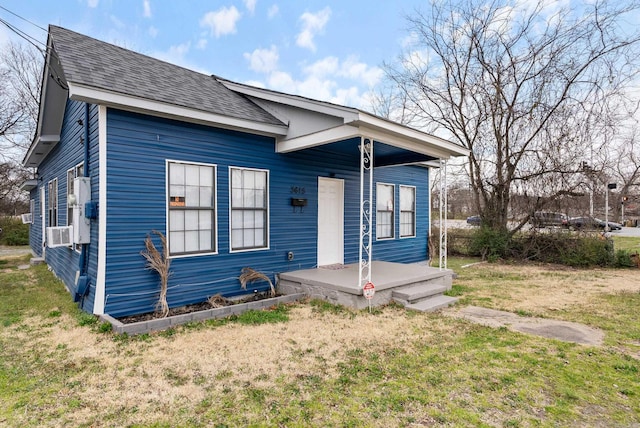 bungalow-style house with cooling unit, roof with shingles, and a front lawn