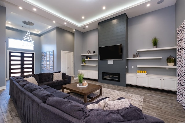 living area with a tray ceiling, wood finished floors, recessed lighting, a fireplace, and baseboards