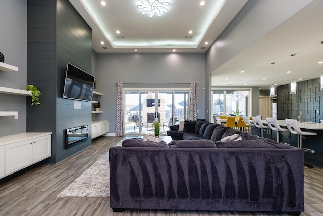 living room with a tray ceiling, recessed lighting, wood finished floors, and a towering ceiling