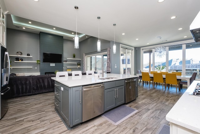 kitchen featuring a center island with sink, gray cabinets, a sink, appliances with stainless steel finishes, and open floor plan