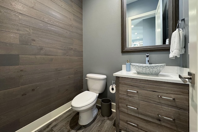 half bathroom with toilet, vanity, baseboards, and wood finished floors