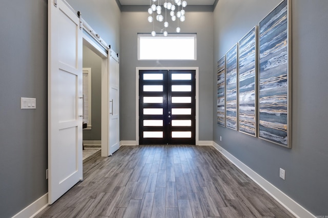 entrance foyer featuring dark wood-style floors, a barn door, french doors, an inviting chandelier, and baseboards