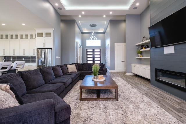 living room with a tray ceiling, a glass covered fireplace, wood finished floors, baseboards, and a towering ceiling