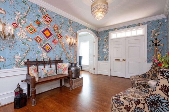 entrance foyer featuring wood finished floors, a wainscoted wall, wallpapered walls, arched walkways, and crown molding