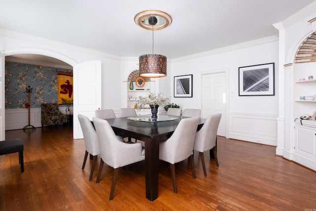 dining space featuring built in shelves, a wainscoted wall, arched walkways, dark wood-type flooring, and crown molding