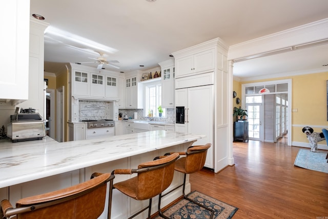 kitchen with a kitchen bar, a peninsula, ornamental molding, and white cabinetry