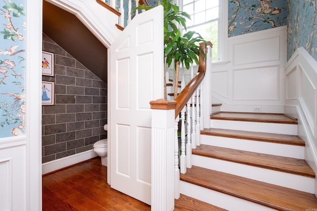 stairway featuring vaulted ceiling, wood finished floors, wainscoting, and wallpapered walls