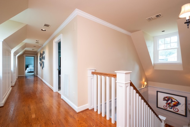 hallway with an upstairs landing, visible vents, crown molding, and light wood-style floors