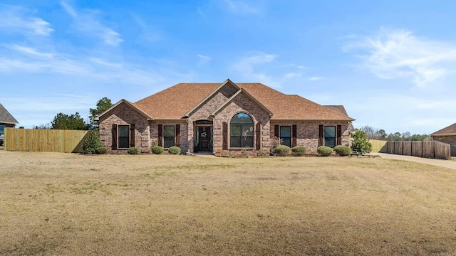 view of front of home featuring brick siding, a front yard, roof with shingles, and fence