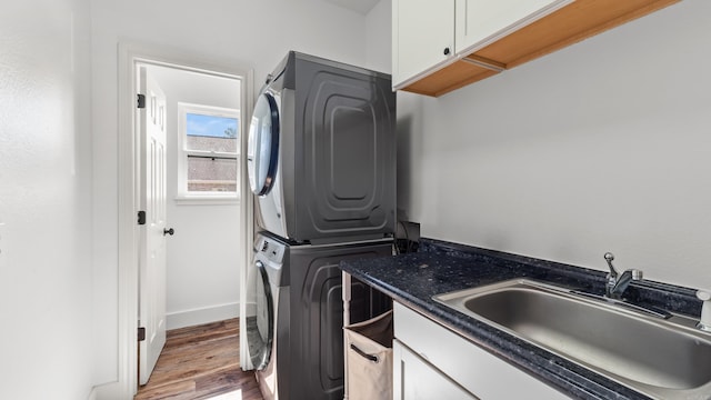 laundry area with baseboards, wood finished floors, cabinet space, stacked washer / drying machine, and a sink