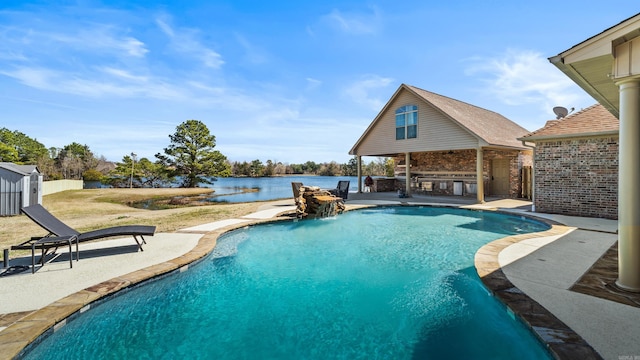 outdoor pool with a patio, an outbuilding, fence, a water view, and outdoor dry bar