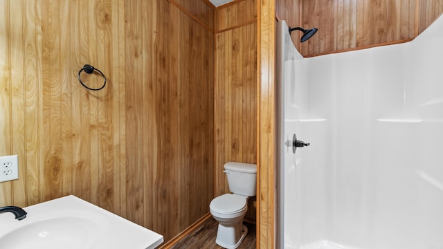 bathroom with wood finished floors, a sink, wood walls, walk in shower, and toilet