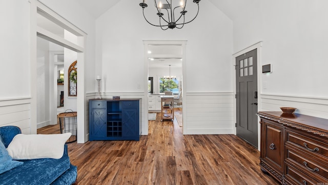 foyer entrance with dark wood finished floors, lofted ceiling, a wainscoted wall, and a chandelier