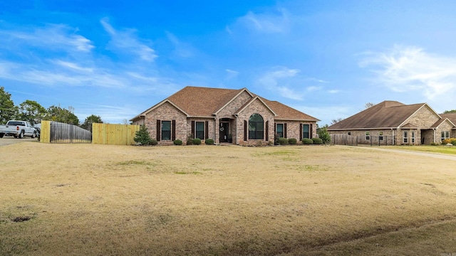 french country inspired facade featuring a gate, fence, brick siding, and a shingled roof