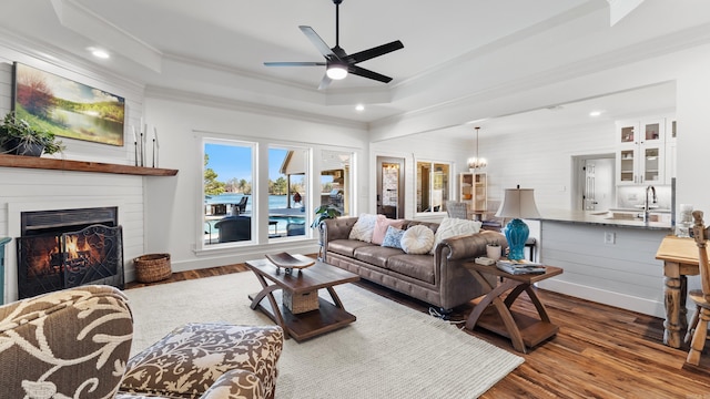 living room featuring ornamental molding, a warm lit fireplace, a raised ceiling, and wood finished floors