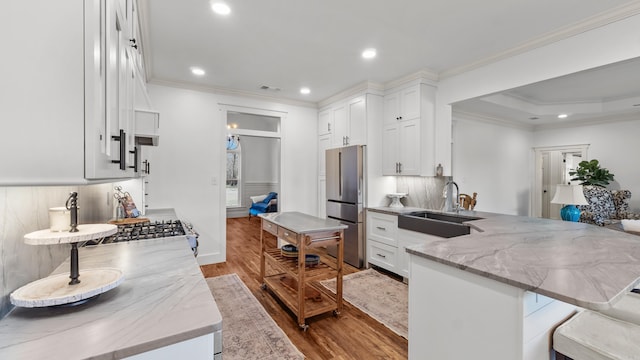 kitchen with a sink, a peninsula, freestanding refrigerator, and ornamental molding