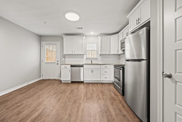 kitchen with tasteful backsplash, visible vents, stainless steel appliances, white cabinetry, and a sink