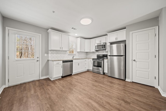 kitchen with a sink, stainless steel appliances, wood finished floors, and decorative backsplash