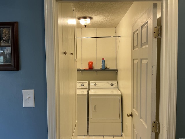 clothes washing area with laundry area, light tile patterned flooring, separate washer and dryer, and a textured ceiling