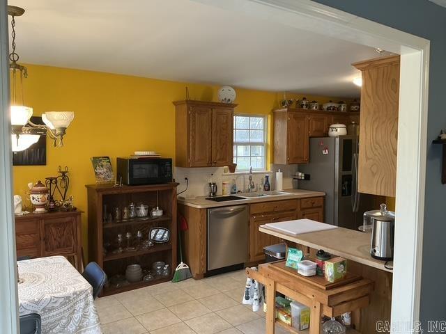 kitchen featuring a sink, stainless steel appliances, light countertops, pendant lighting, and brown cabinets