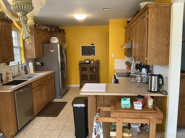 kitchen with a sink, tasteful backsplash, appliances with stainless steel finishes, light countertops, and light tile patterned floors