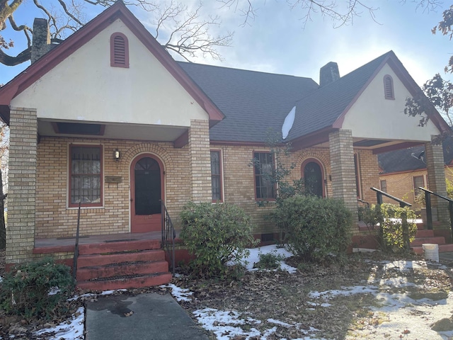 tudor home with brick siding, stucco siding, a chimney, and roof with shingles