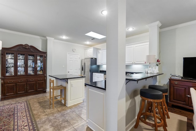 kitchen featuring a kitchen bar, dark countertops, stainless steel fridge, white cabinets, and crown molding