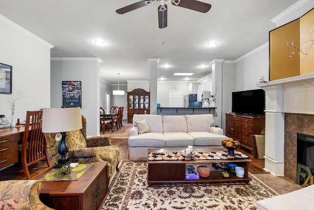 living area with recessed lighting, wood finished floors, a tiled fireplace, and crown molding