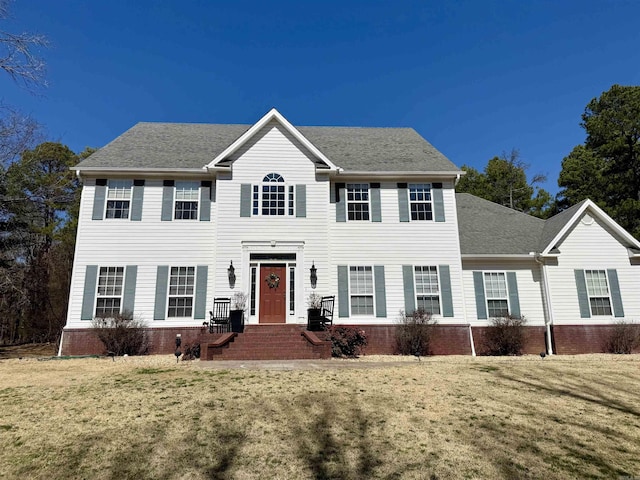 colonial house featuring a front lawn and roof with shingles