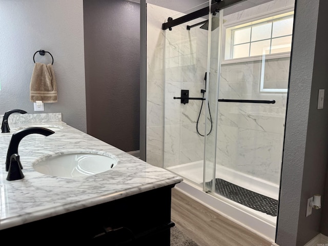 bathroom featuring a sink, wood finished floors, a marble finish shower, double vanity, and a textured wall