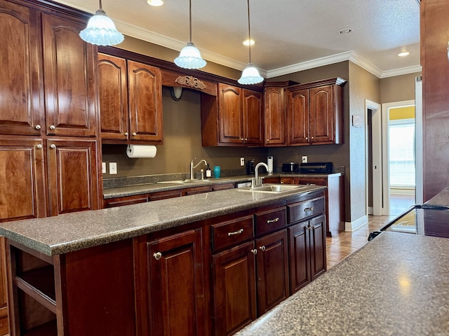 kitchen with a sink, an island with sink, ornamental molding, and hanging light fixtures