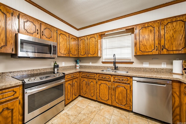 kitchen with brown cabinets, ornamental molding, a sink, a textured ceiling, and stainless steel appliances