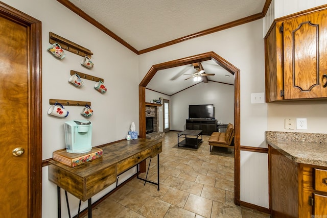 home office featuring a ceiling fan, ornamental molding, vaulted ceiling, a textured ceiling, and a brick fireplace