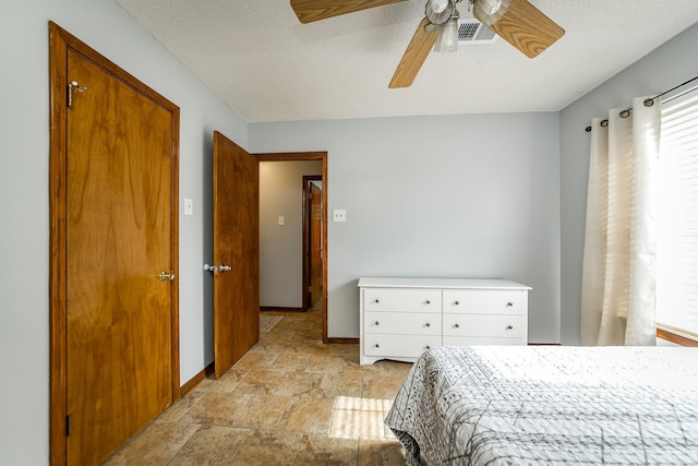 bedroom with a ceiling fan, visible vents, baseboards, stone finish flooring, and a textured ceiling