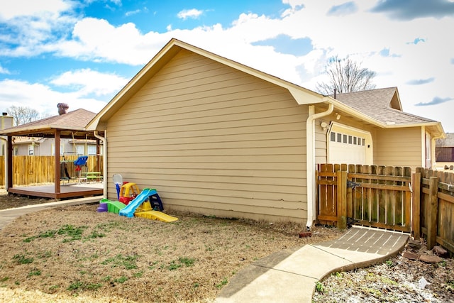 view of side of property with a garage, a wooden deck, roof with shingles, and fence