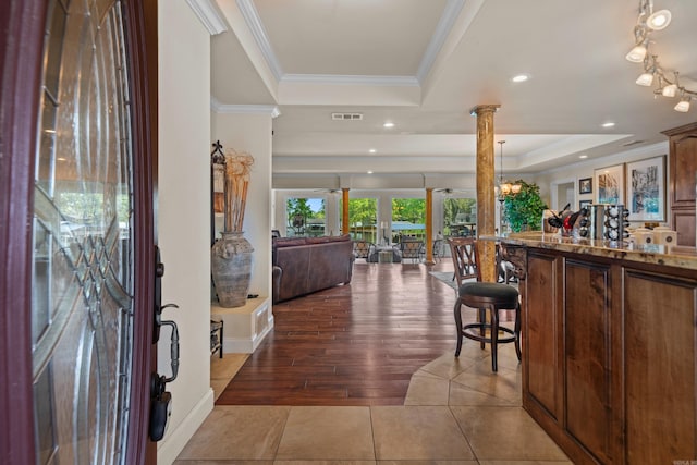 foyer entrance with visible vents, a tray ceiling, decorative columns, ornamental molding, and tile patterned floors