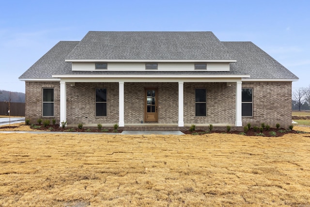 rear view of house with a yard, brick siding, covered porch, and a shingled roof