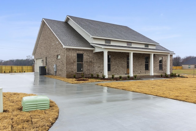 view of front of home with brick siding, a shingled roof, a porch, central AC unit, and driveway