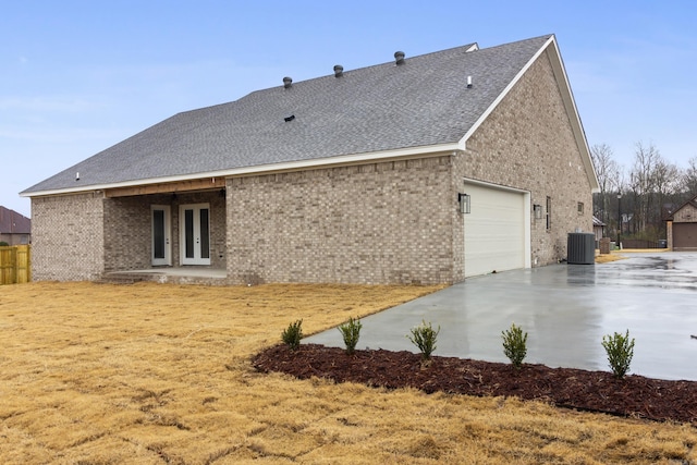 rear view of property with french doors, brick siding, central AC, and driveway