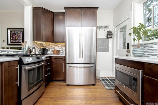 kitchen with dark brown cabinets, backsplash, stainless steel appliances, and light wood-type flooring