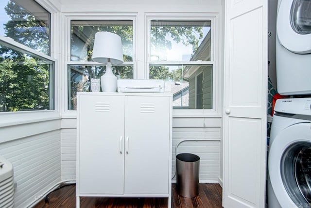 clothes washing area featuring dark wood finished floors, stacked washer / dryer, and a healthy amount of sunlight