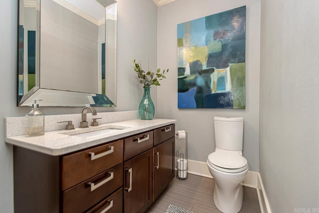 half bathroom with vanity, crown molding, toilet, and baseboards