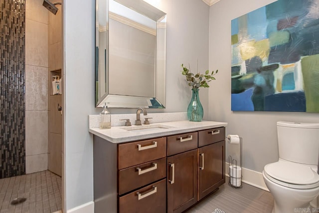 bathroom featuring a tile shower, toilet, vanity, and baseboards