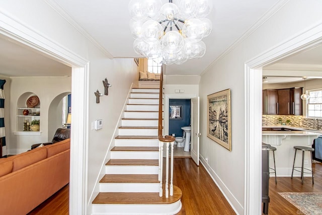 stairway featuring arched walkways, an inviting chandelier, wood finished floors, and ornamental molding