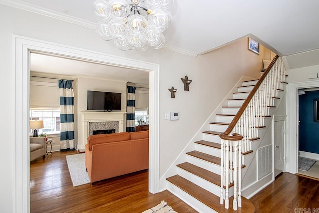 staircase featuring visible vents, wood finished floors, a fireplace, and crown molding